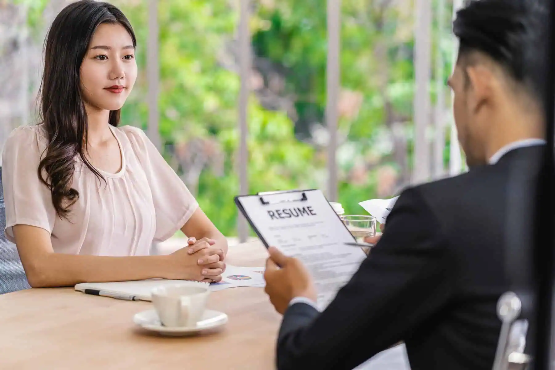 A woman attends a job interview while the interviewer reviews her résumé across a desk.