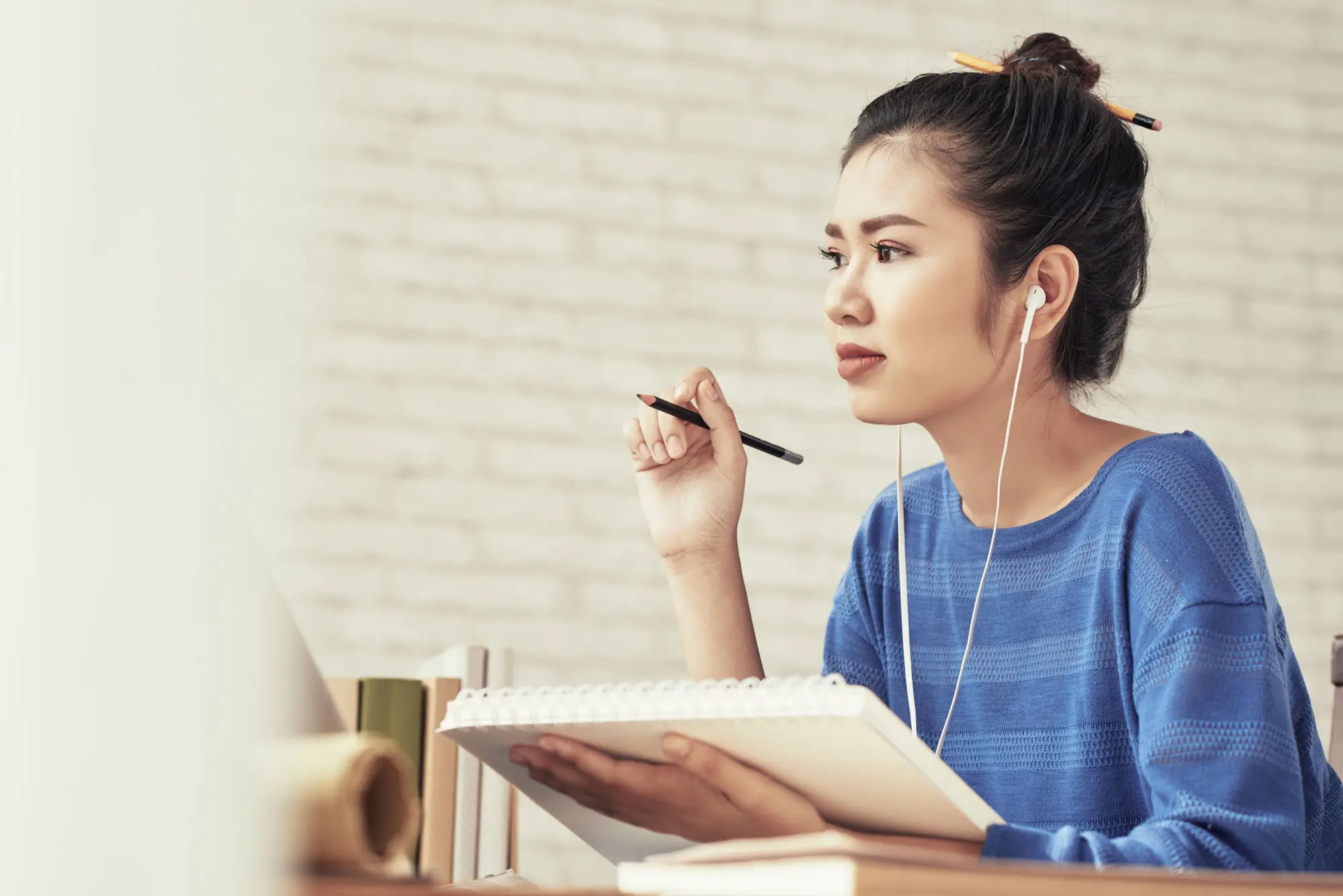 A woman attends an online class while taking notes in a notebook.