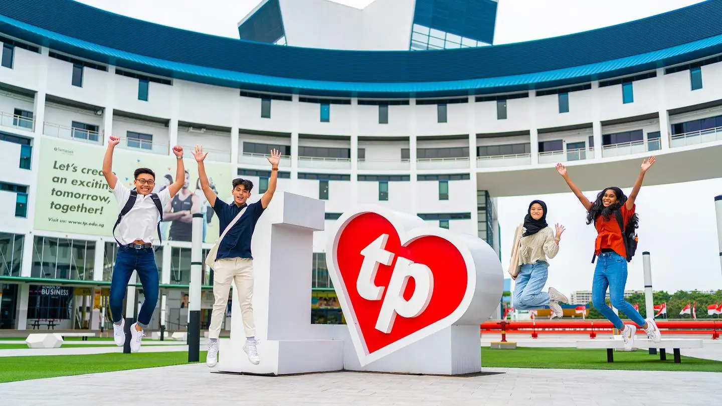 A group of four diverse Temasek Polytechnic students are seen mid-jump in front of Temasek Polytechnic’s central administration building. They are smiling and appear joyful, showcasing school pride and unity.