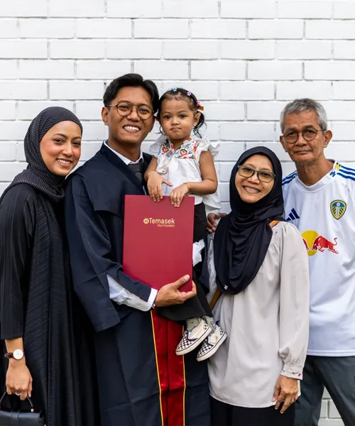 Muhammad Khairi Mohamad Shah, in graduation gown, holds his Temasek Polytechnic diploma folder while posing with his family, including his mother, after completing his diploma 20 years after leaving polytechnic.
