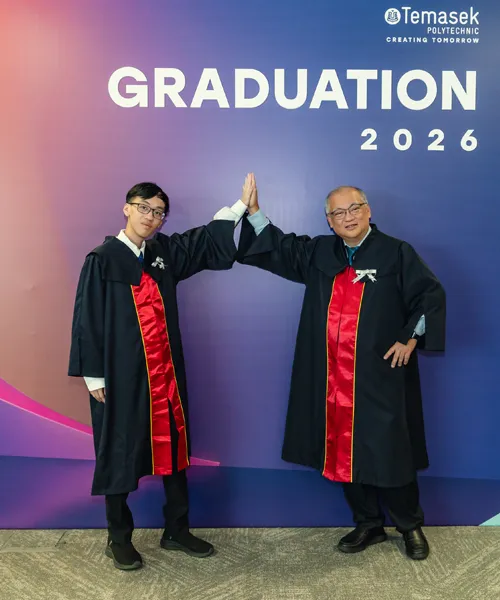 Mr Tay Tse Wan and his son, Tay Quan Kai, in graduation gowns, high-five at Temasek Polytechnic’s Graduation 2026 after completing their Specialist Diploma in AI Solutions Development together.