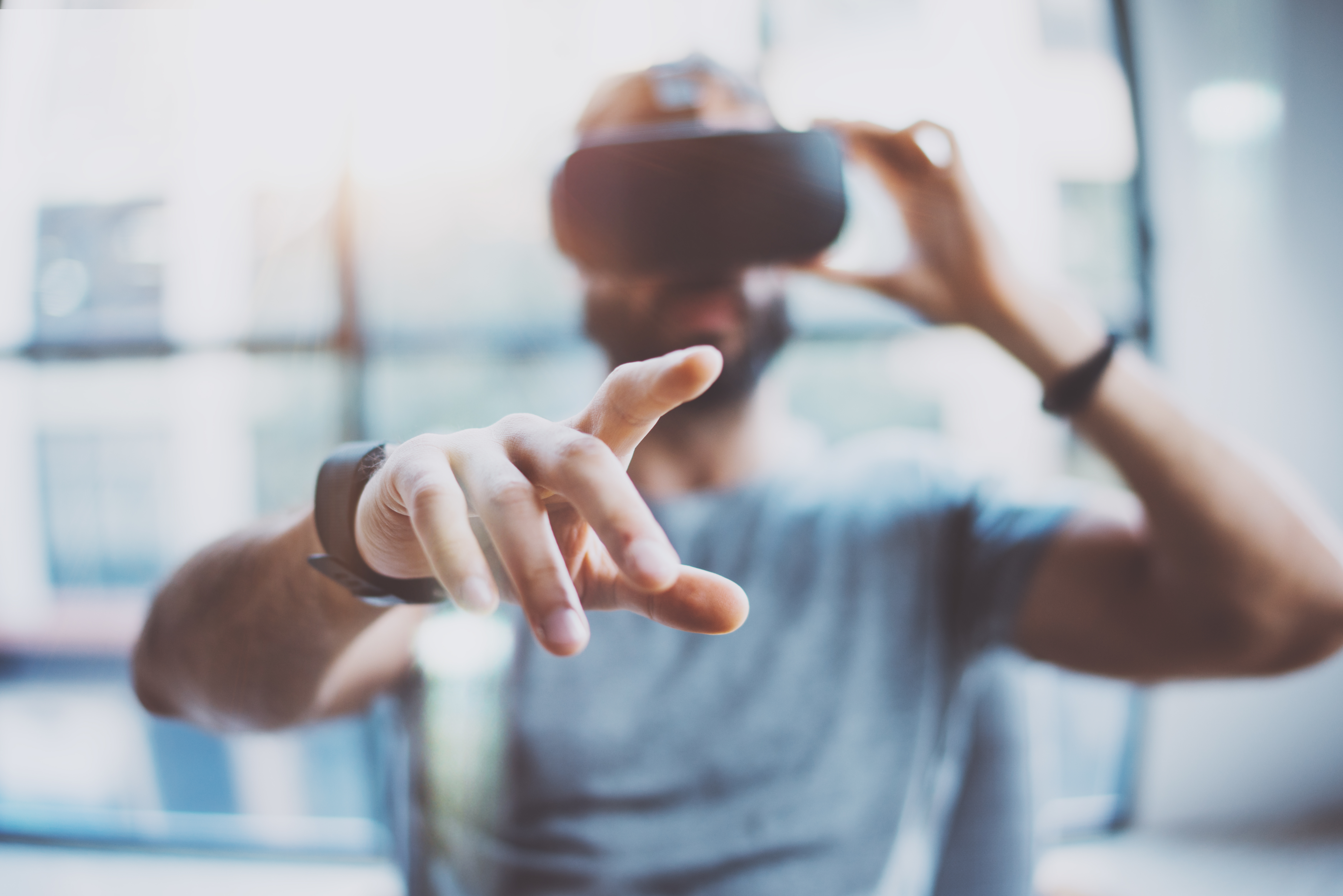 Closeup of male hand.Bearded young man wearing virtual reality goggles in modern coworking studio. Smartphone using with VR headset in office. Horizontal, blurred